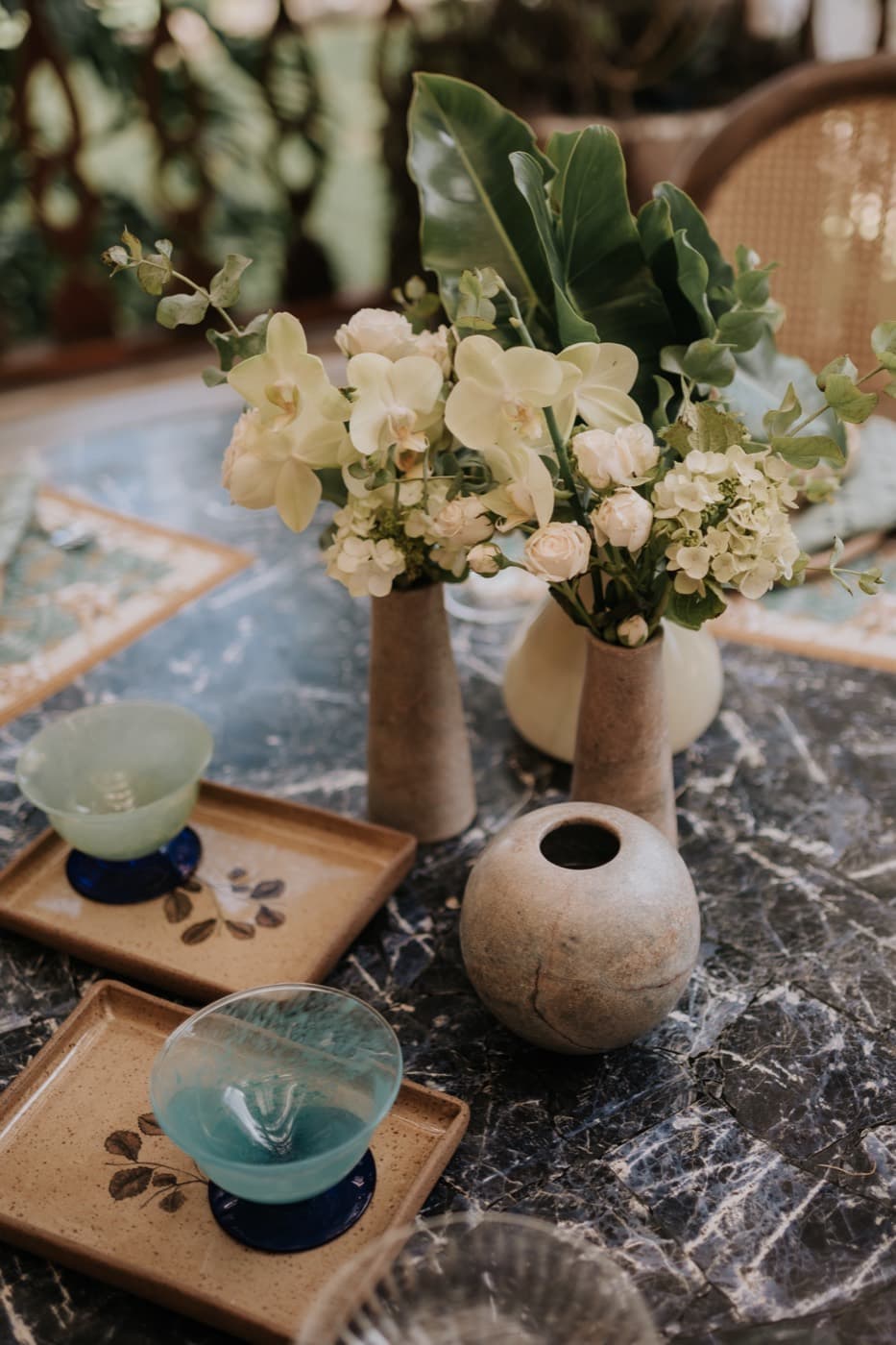 Mesa com arranjo de orquídeas, vasos de pedra e taças azuis sobre bandejas de cerâmica