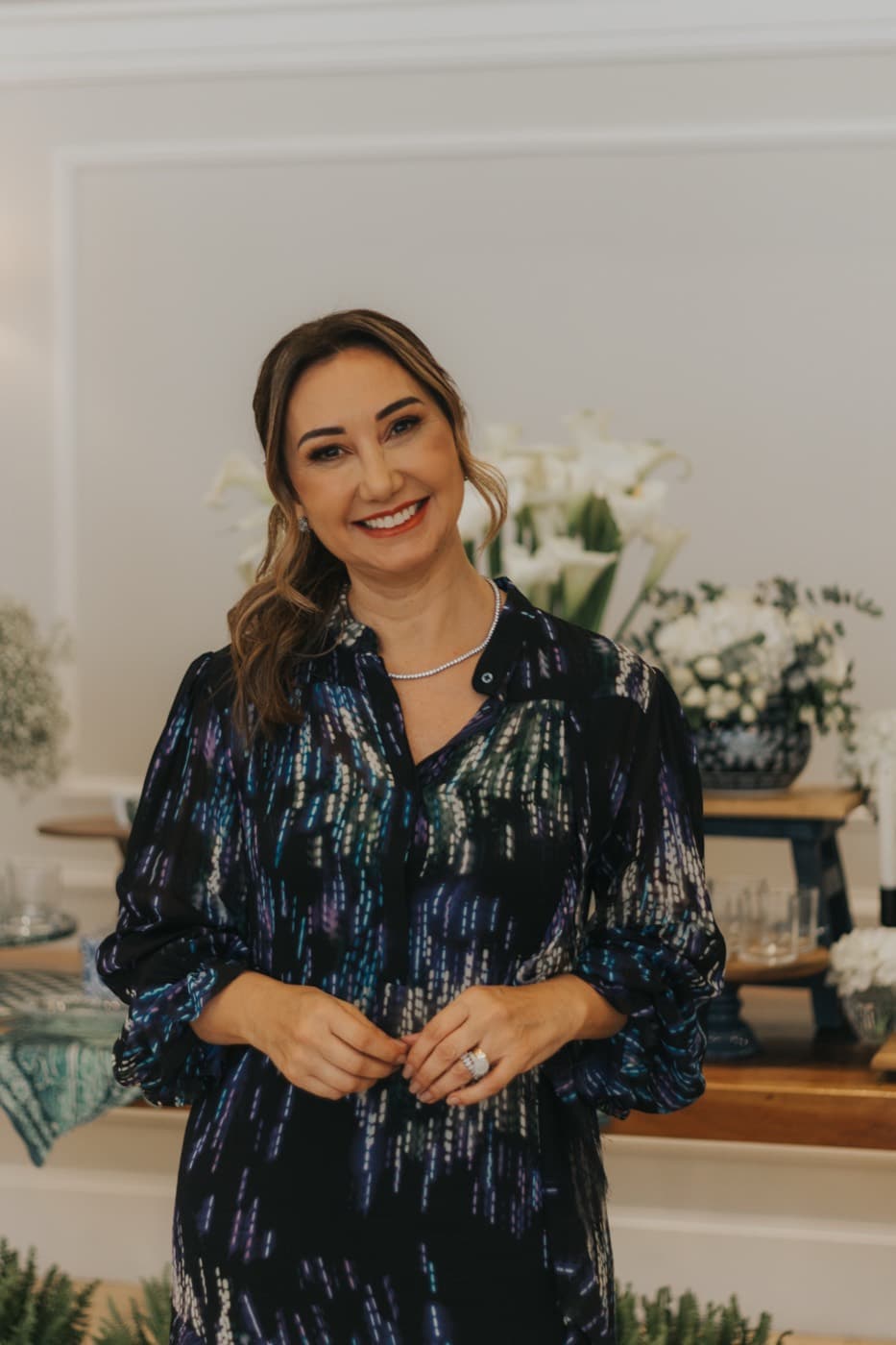 Retrato de Carina Verdinelli sorrindo em ambiente decorado com flores brancas